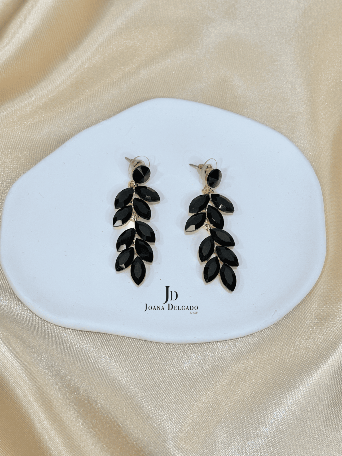 Pendiente metálico en color dorado con piedras negras.