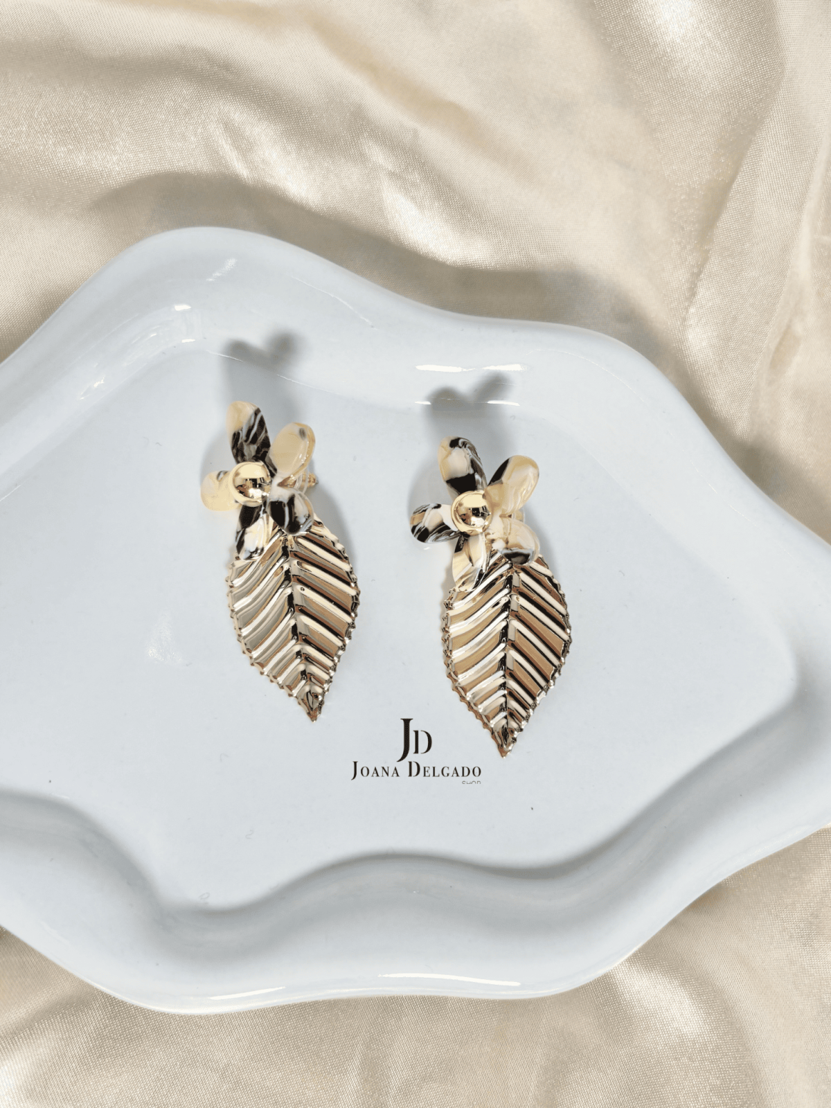 Pendientes con flor efecto nacarado y hoja colgante dorada.