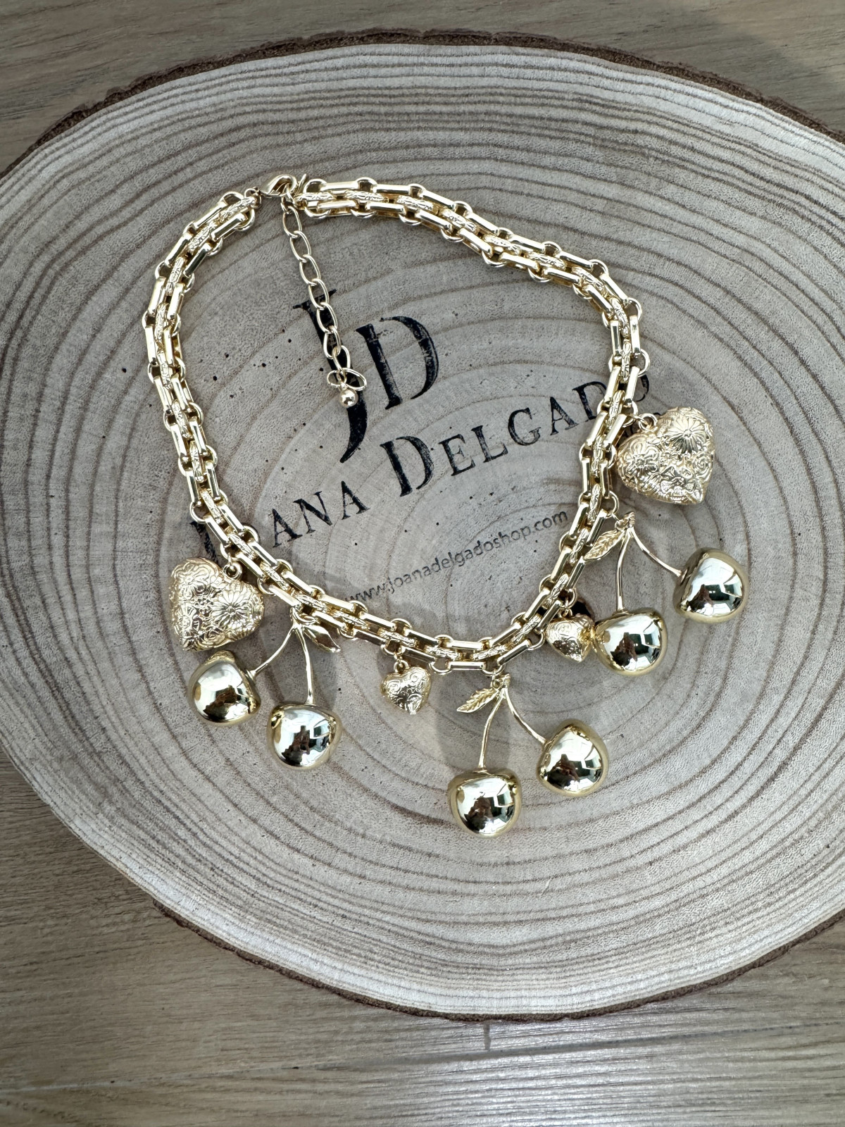 Collar metálico dorado con adornos en forma de cerezas y corazones.