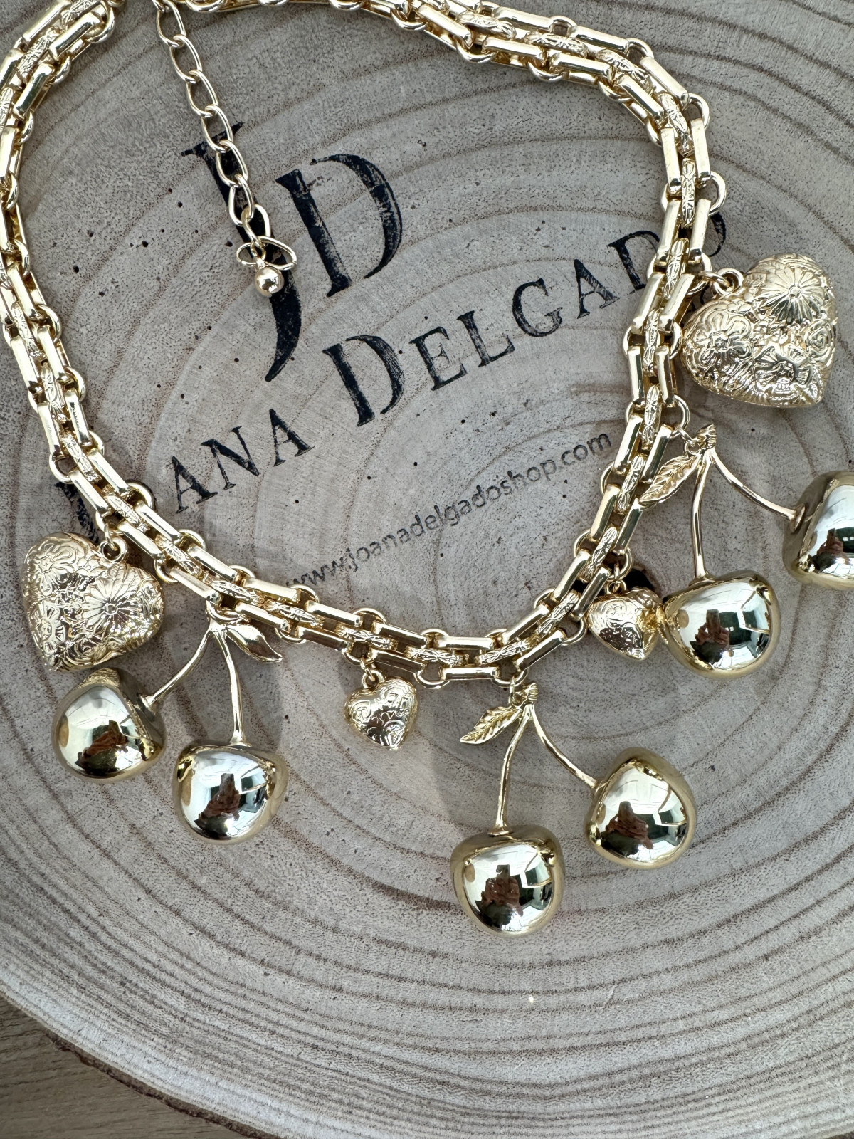Collar metálico dorado con adornos en forma de cerezas y corazones.