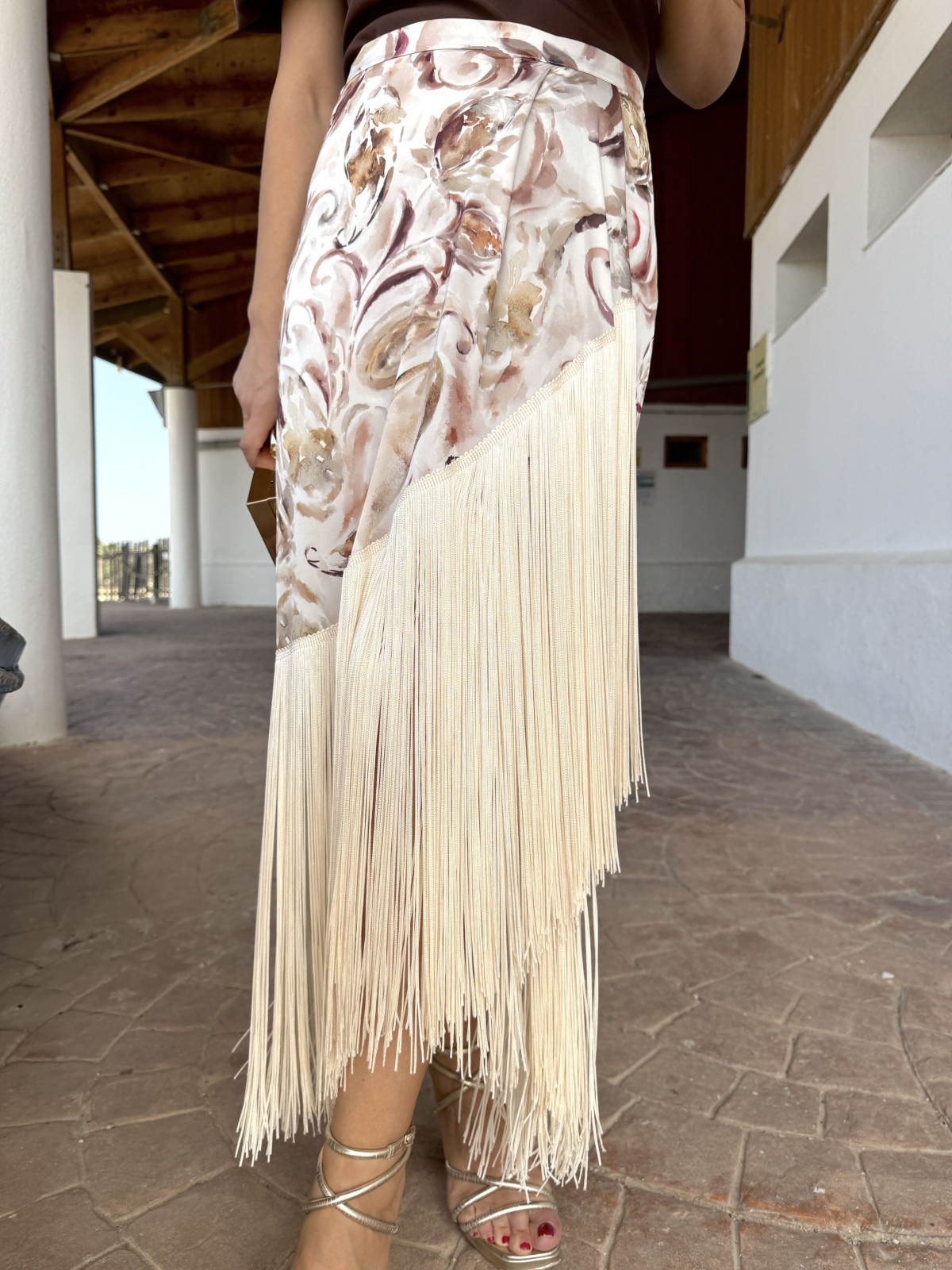 Falda de fiesta en tejido satinado estampado y adornada con flecos.