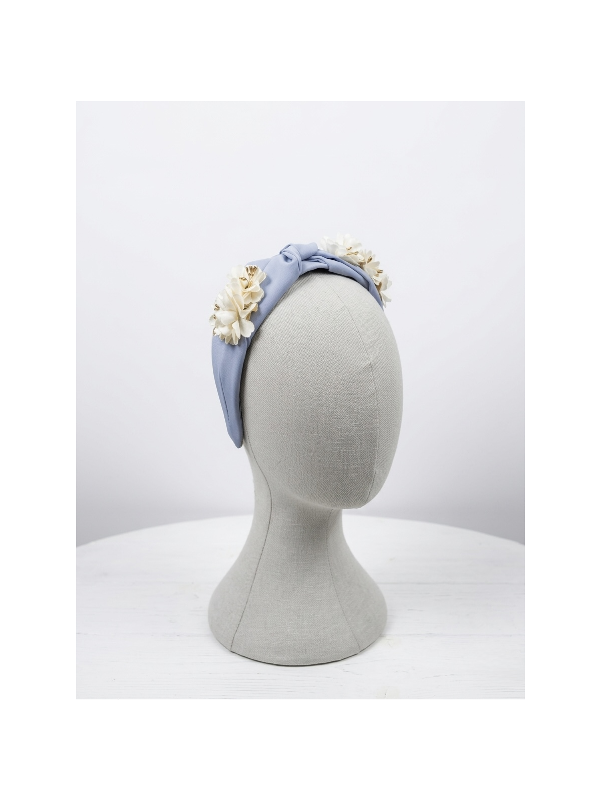 Diadema en tono celeste con delicado nudo central, adornada con flores