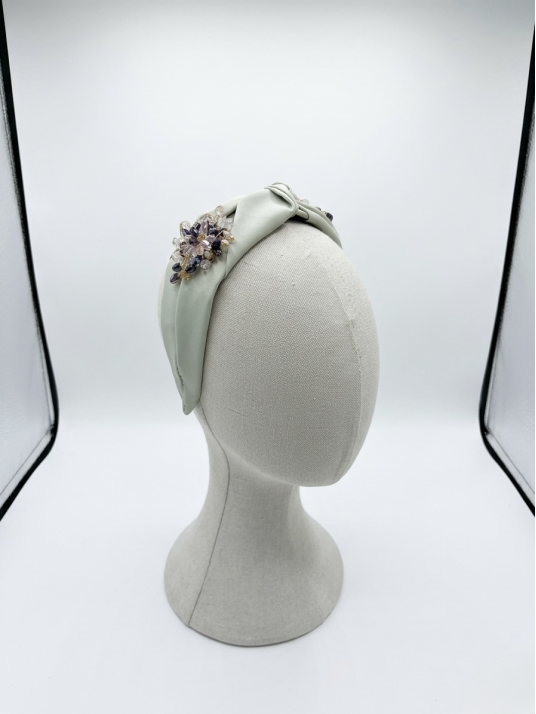 Diadema en tono verde suave con elegante nudo central, adornada con un