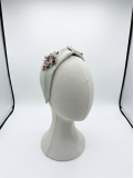 Diadema en tono verde suave con elegante nudo central, adornada con un