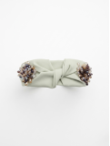 Diadema en tono verde suave con elegante nudo central, adornada con un